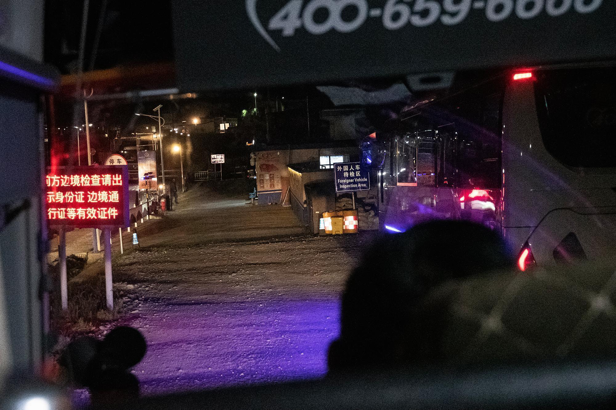 A view from inside a vehicle at night approaching a tibetan border inspection area with signs in Chinese and English.