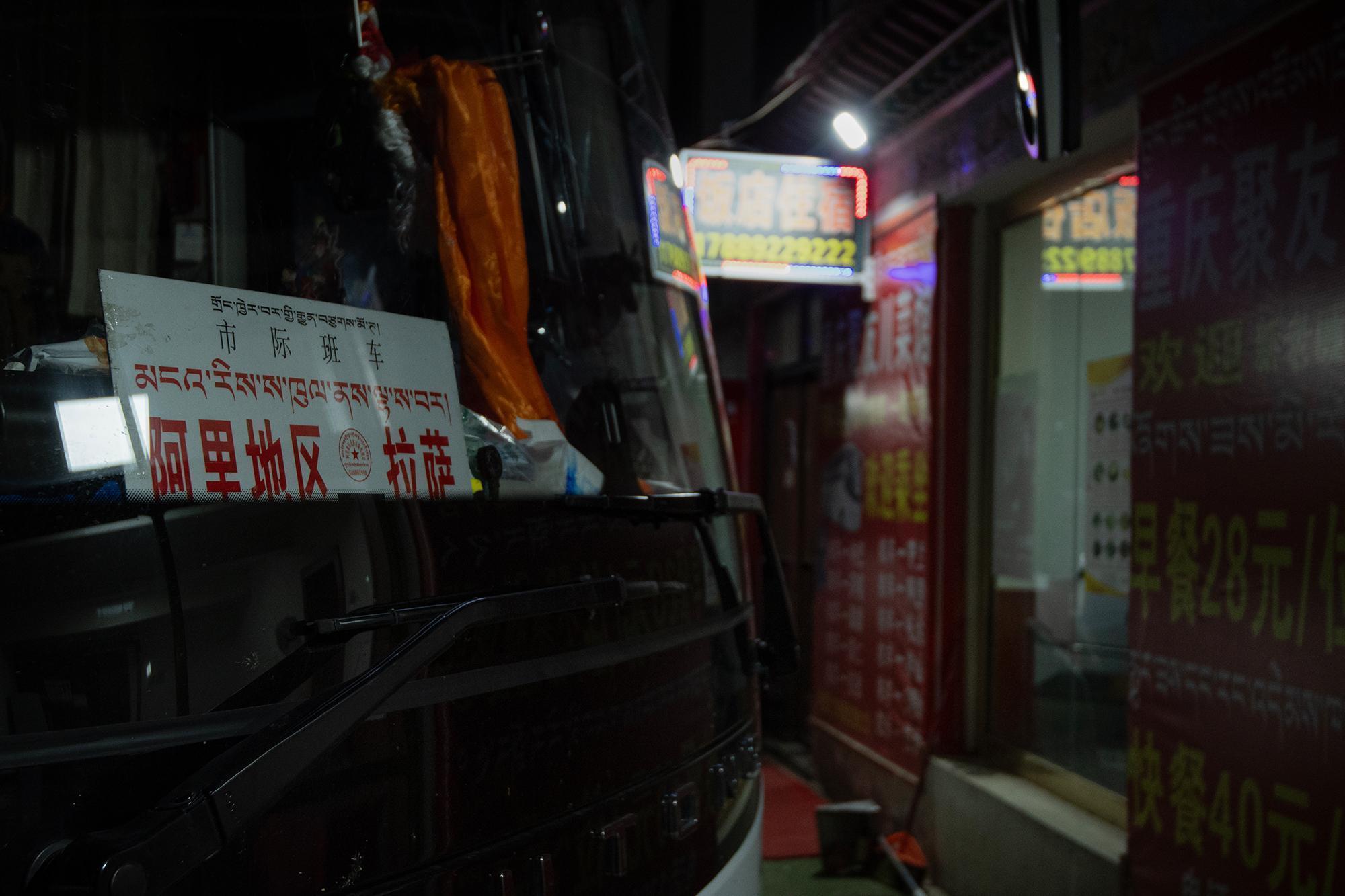 Bus stopped at a restaurant around midnight, with a sign in Chinese and Tibetan visible through the front window.