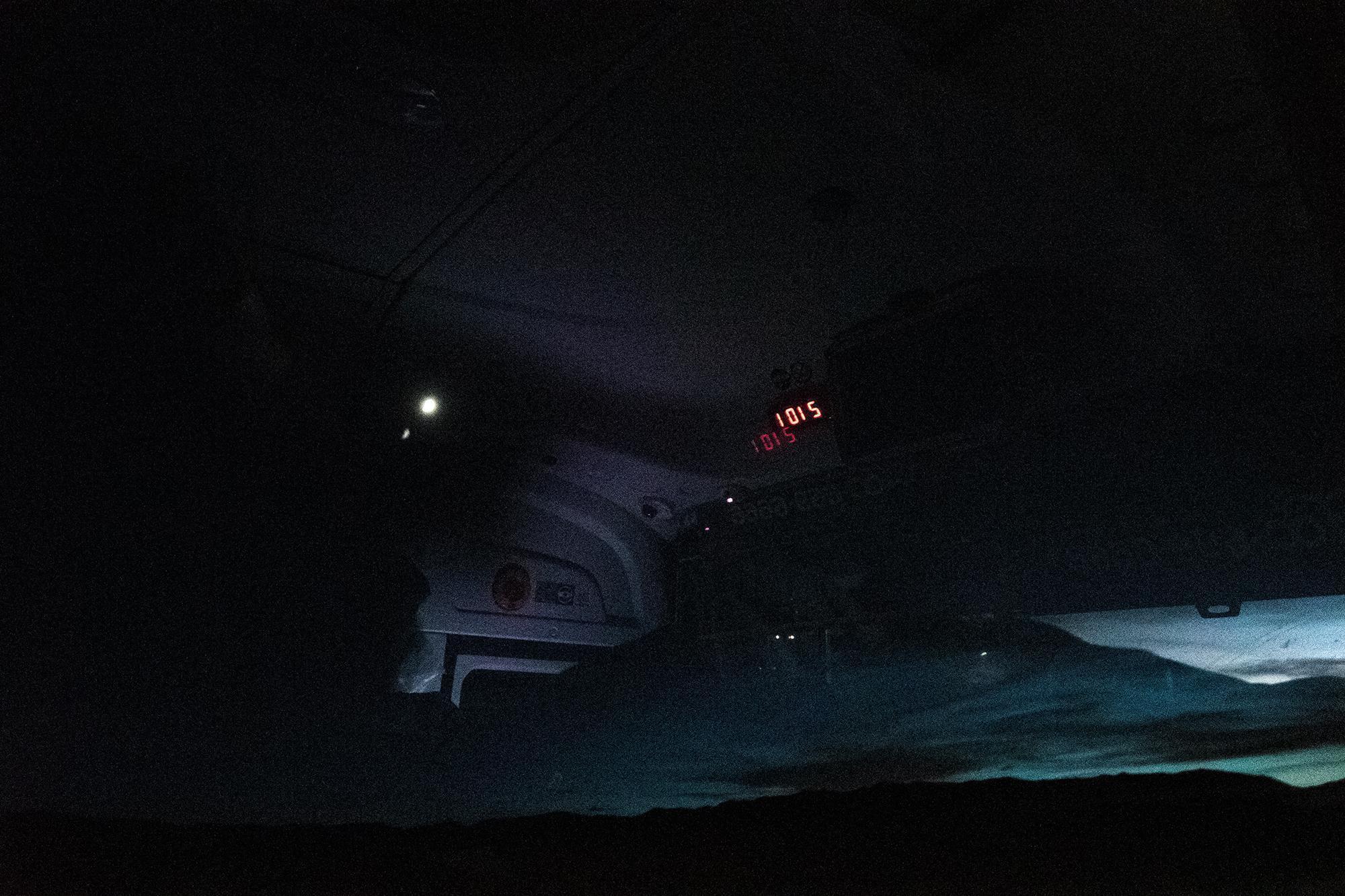 Dark bus interior at dusk, with mirrored red digits 2101 displayed overhead and a dimly lit landscape visible through the window.