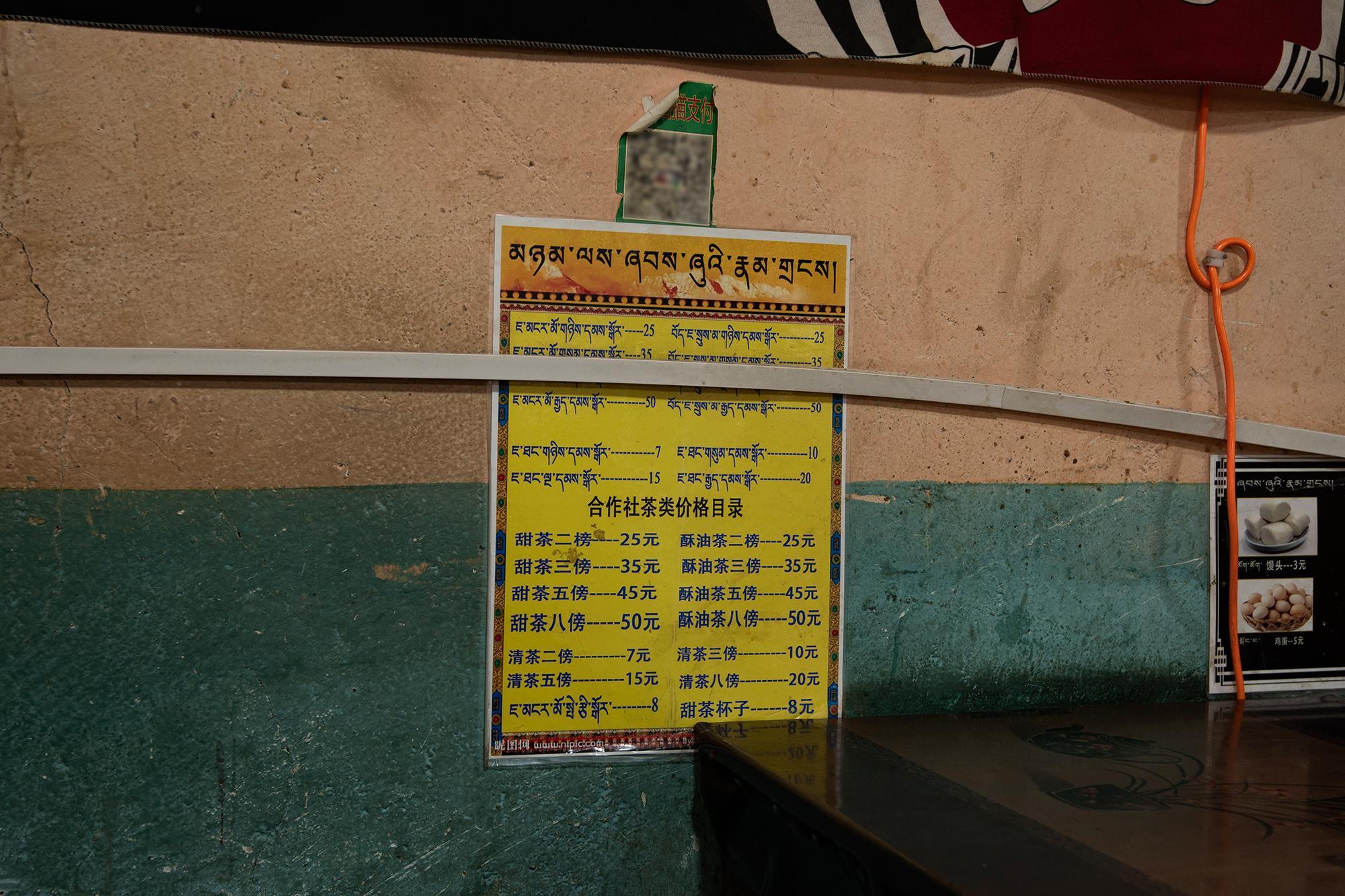 Yellow menu with Tibetan and Chinese text showing prices for sweet, butter, and plain tea, with smaller signs for steamed buns and eggs.